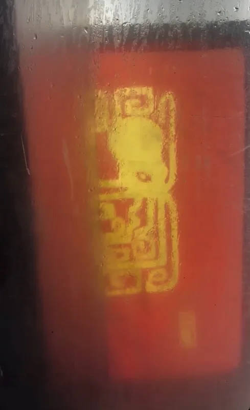 Rood-oranje vlak achter beslagen glas met een geel grafisch symbool.